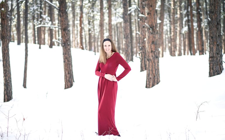 A woman in a red coat standing against the hush of winter snow, a bold flame of colour.